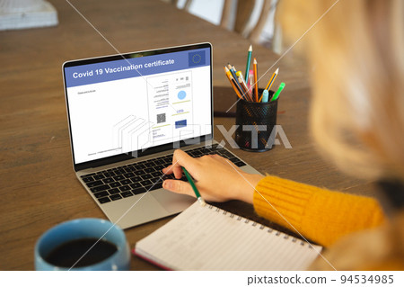 Caucasian woman using laptop with covid vaccination certificate and qr code on screen 94534985