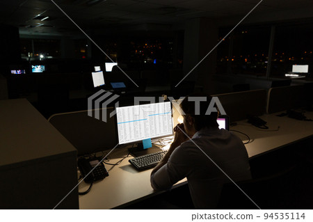 Caucasian male programmer sitting at desk, using computer with coding on screen Caucasian male programmer sitting at desk, using computer with coding on screen 94535114