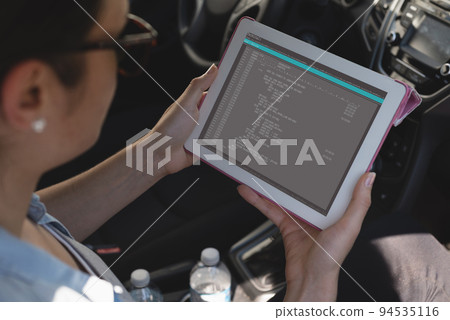 Biracial female programmer sitting in car, holding tablet with coding on screen Biracial female programmer sitting in car, holding tablet with coding on screen 94535116