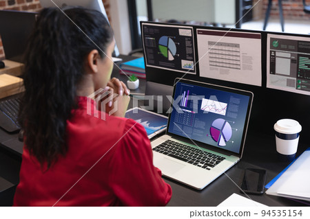 Biracial businesswoman sitting at desk using laptop with graph and statistical data on screen Biracial businesswoman sitting at desk using laptop with graph and statistical data on screen 94535154
