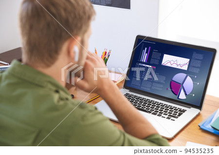 Caucasian businessman sitting at desk using laptop with graph and statistical data on screen Caucasian businessman sitting at desk using laptop with graph and statistical data on screen 94535235