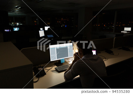 Caucasian male programmer sitting at desk and using computer with coding on screen Caucasian male programmer sitting at desk and using computer with coding on screen 94535280
