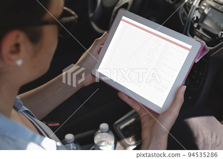 Biracial female programmer sitting in car and using tablet with coding on screen Biracial female programmer sitting in car and using tablet with coding on screen 94535286