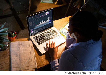 Biracial businesswoman sitting at desk using laptop with statistical data on screen Biracial businesswoman sitting at desk using laptop with statistical data on screen 94535313