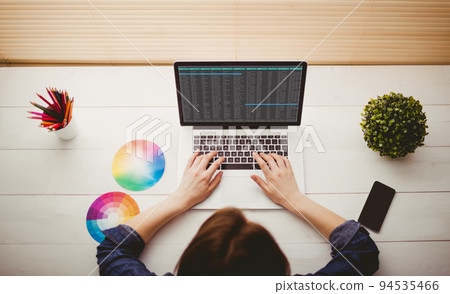 Caucasian female programmer sitting at desk with colour charts, using laptop with coding on screen Caucasian female programmer sitting at desk with colour charts, using laptop with coding on screen 94535466