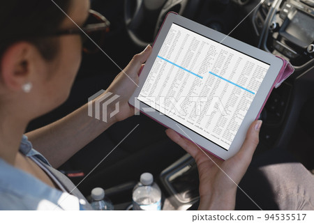 Biracial female programmer sitting in car, using tablet with coding on screen Biracial female programmer sitting in car, using tablet with coding on screen 94535517