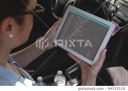Biracial female programmer sitting in car, using tablet with coding on screen Biracial female programmer sitting in car, using tablet with coding on screen 94535518