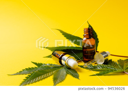 Image of bottle of cbd oil and marihuana leaves on yellow surface 94536026