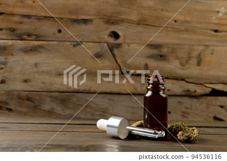 Image of bottle of cbd oil and dried marihuana leaves on wooden surface 94536116