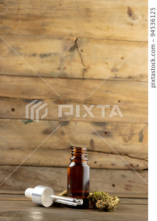 Vertical image of bottle of cbd oil and dried marihuana leaves on wooden surface Vertical image of bottle of cbd oil and dried marihuana leaves on wooden surface 94536125