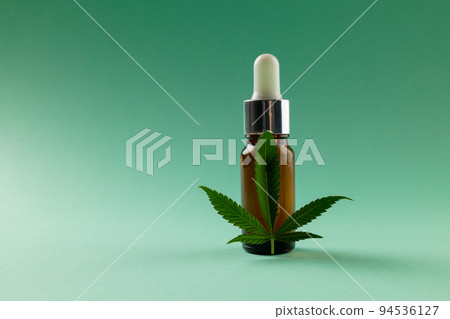 Image of bottle of cbd oil and marihuana leaf on green surface Image of bottle of cbd oil and marihuana leaf on green surface 94536127