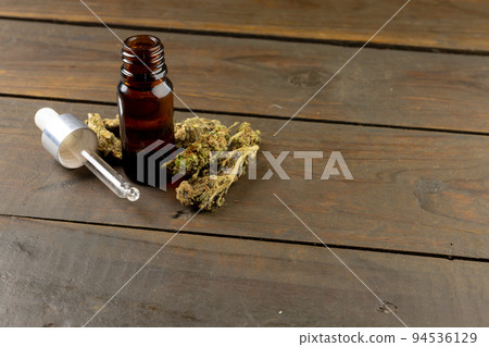 Image of bottle of cbd oil and dried marihuana leaves on wooden surface Image of bottle of cbd oil and dried marihuana leaves on wooden surface 94536129