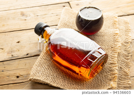 Horizontal image of glass bottle and bowl of maple syrup on sackcloth on wooden table 94536603