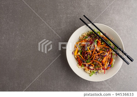 Overhead view of asian wok stir fry and chopsticks with copy space on grey background Overhead view of asian wok stir fry and chopsticks with copy space on grey background 94536633