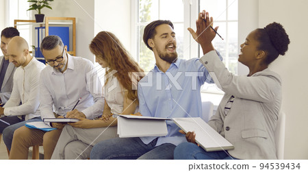 Cheerful colleagues give each other after successfully completed task at business training. Cheerful colleagues give each other after successfully completed task at business training. 94539434