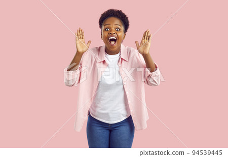 Overjoyed African American woman screams WoW seeing unexpected surprise stands on pink background 94539445
