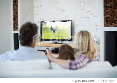 Rear view of family sitting at home together watching golf event on tv Rear view of family sitting at home together watching golf event on tv 94540288