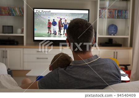 Rear view of father and son sitting at home together watching sport event on tv 94540409