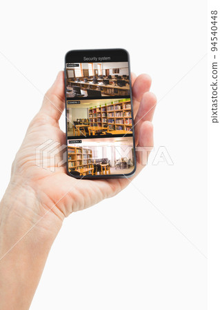 Hand of caucasian man holding smartphone with view from security cameras at library on screen Hand of caucasian man holding smartphone with view from security cameras at library on screen 94540448