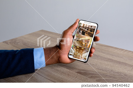 Hand of caucasian man holding smartphone with view from security cameras at library on screen 94540462
