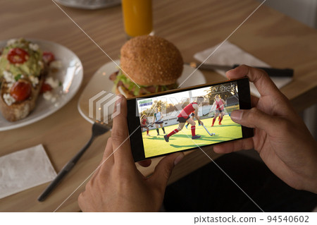 Hands of african american man at restaurant watching hockey match on smartphone 94540602