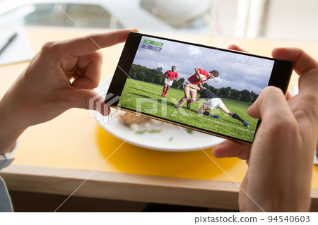 Hands of caucasian man at restaurant watching rugby match on smartphone 94540603