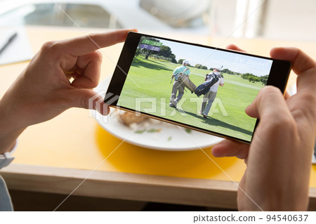 Hands of caucasian man at restaurant watching golf match on smartphone 94540637