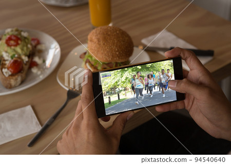 Hands of caucasian man at restaurant watching marathon runners on smartphone Hands of caucasian man at restaurant watching marathon runners on smartphone 94540640