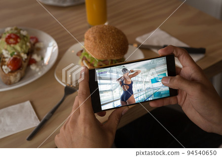 Hands of african american man at restaurant watching female swimmer on smartphone Hands of african american man at restaurant watching female swimmer on smartphone 94540650