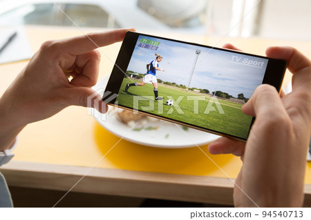 Hands of caucasian man at restaurant watching soccer match on smartphone Hands of caucasian man at restaurant watching soccer match on smartphone 94540713