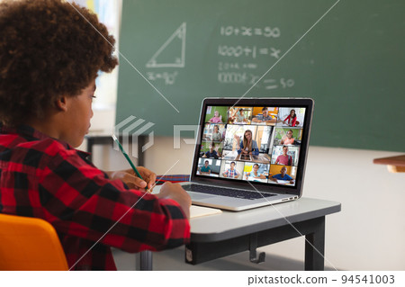 African american boy using laptop for video call, with diverse elementary school pupils on screen 94541003