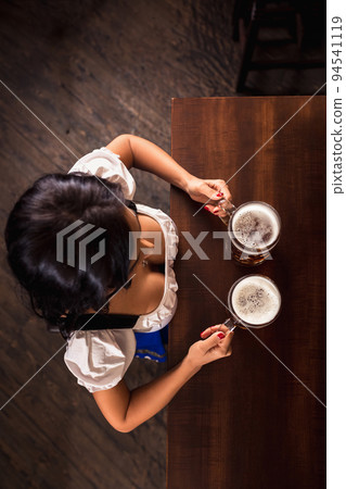 Oktoberfest. Brunette woman holding beer mugs in bar. Top view Oktoberfest. Brunette woman holding beer mugs in bar. Top view 94541119