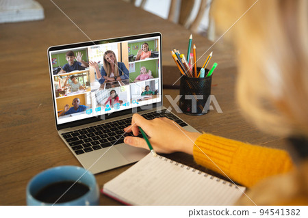 Caucasian woman using laptop for video call, with diverse elementary school pupils on screen 94541382