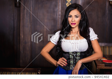 Oktoberfest woman wearing a traditional Bavarian dress dirndl posing at bar Oktoberfest woman wearing a traditional Bavarian dress dirndl posing at bar 94541402