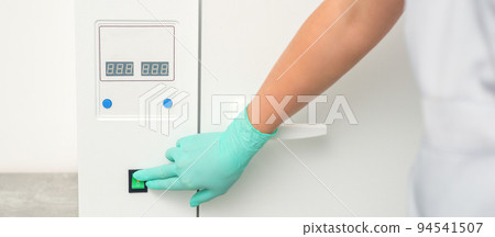 Beautician in protective gloves starts the machine for disinfection of tools before the medical procedure 94541507