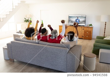 Rear view of family sitting at home together watching sport event on tv Rear view of family sitting at home together watching sport event on tv 94541508