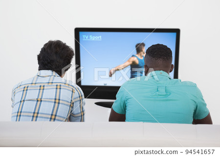 Rear view of two friends sitting at home together watching sport event on tv 94541657