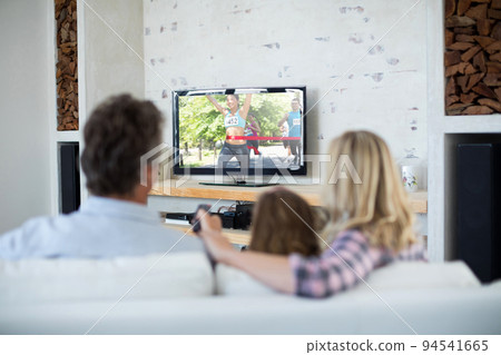 Rear view of family sitting at home together watching athletics event on tv 94541665