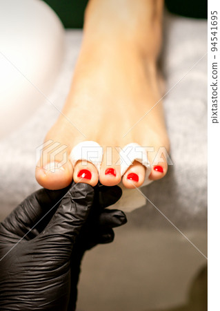 Nail painting process. A manicure master hand holds red painted fingernails on a female leg in a beauty salon 94541695