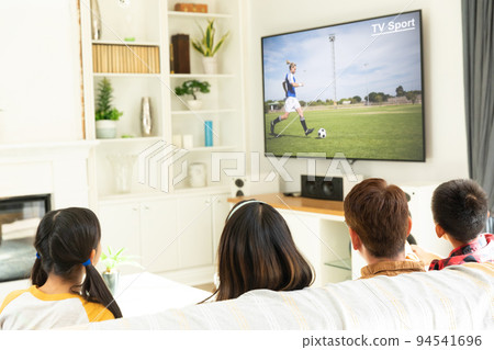 Rear view of family sitting at home together watching football match on tv 94541696