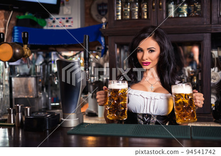 Oktoberfest. Brunette woman holding beer mugs in bar Oktoberfest. Brunette woman holding beer mugs in bar 94541742