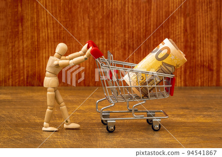 Wooden dummy pushing shopping cart with a money roll Wooden dummy pushing shopping cart with a money roll 94541867