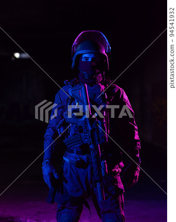 Army soldier in Combat Uniforms with an assault rifle and combat helmet night mission dark background. Blue and purple gel light effect.  94541932