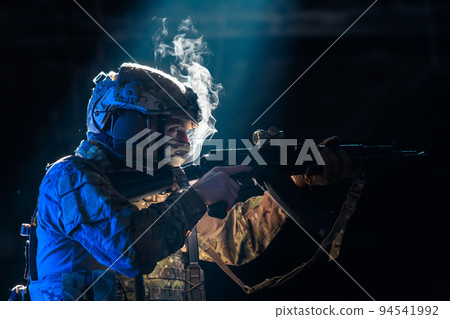Army soldier in Combat Uniforms with an assault rifle and combat helmet night mission dark background. Blue and purple gel light effect.  94541992