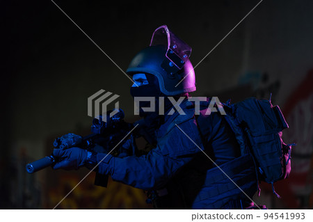 Army soldier in Combat Uniforms with an assault rifle and combat helmet night mission dark background. Blue and purple gel light effect.  94541993