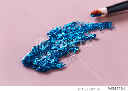Blue glitter cosmetic product smear and brush on pink background. Eye shadow, lip gloss and face for holiday makeup swatch 94542384