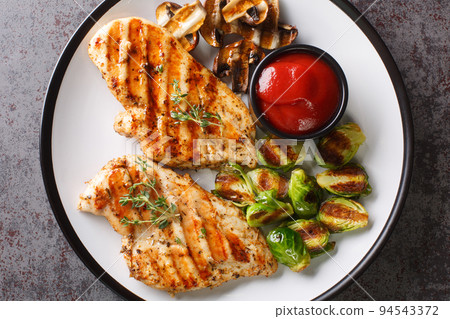 Grilled marinated healthy chicken breasts cooked on a summer barbecue and served with brussels sprouts and mushrooms close-up in a plate. horizontal top view 94543372