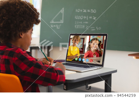 African american boy using laptop for video call, with caucasian elementary school pupils on screen 94544259