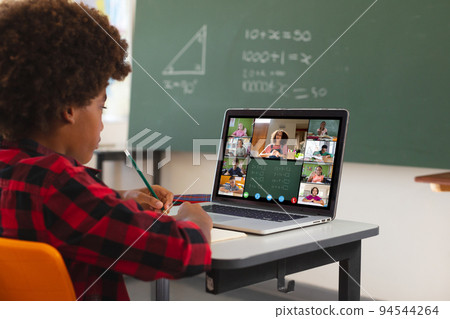 African american boy using laptop for video call, with diverse elementary school pupils on screen 94544264