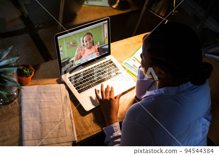 African american woman using laptop for video call, with waving elementary school pupil on screen African american woman using laptop for video call, with waving elementary school pupil on screen 94544384